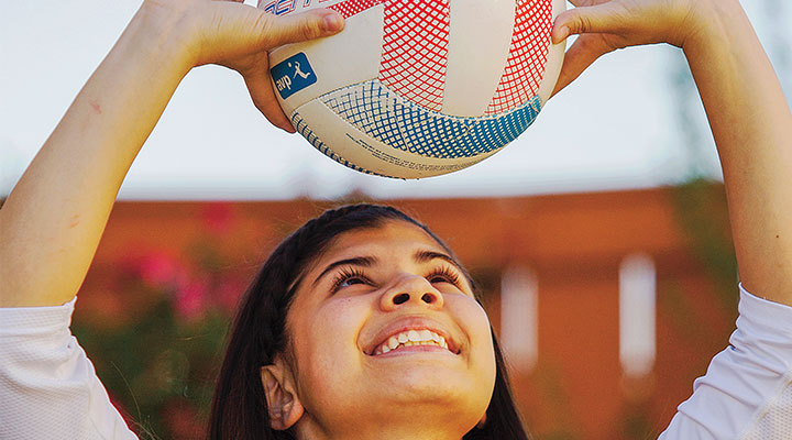 Angelica Torres holds a volleyball over her head.