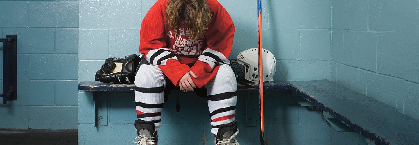 Hockey playing on bench sitting with his head down